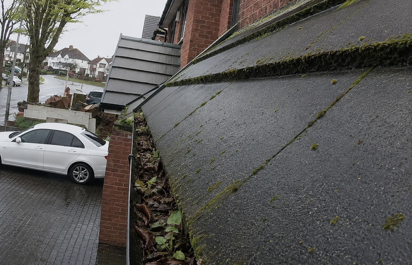 Blocked gutter before Birmingham heavy rain season — leaf debris and weeds in channel